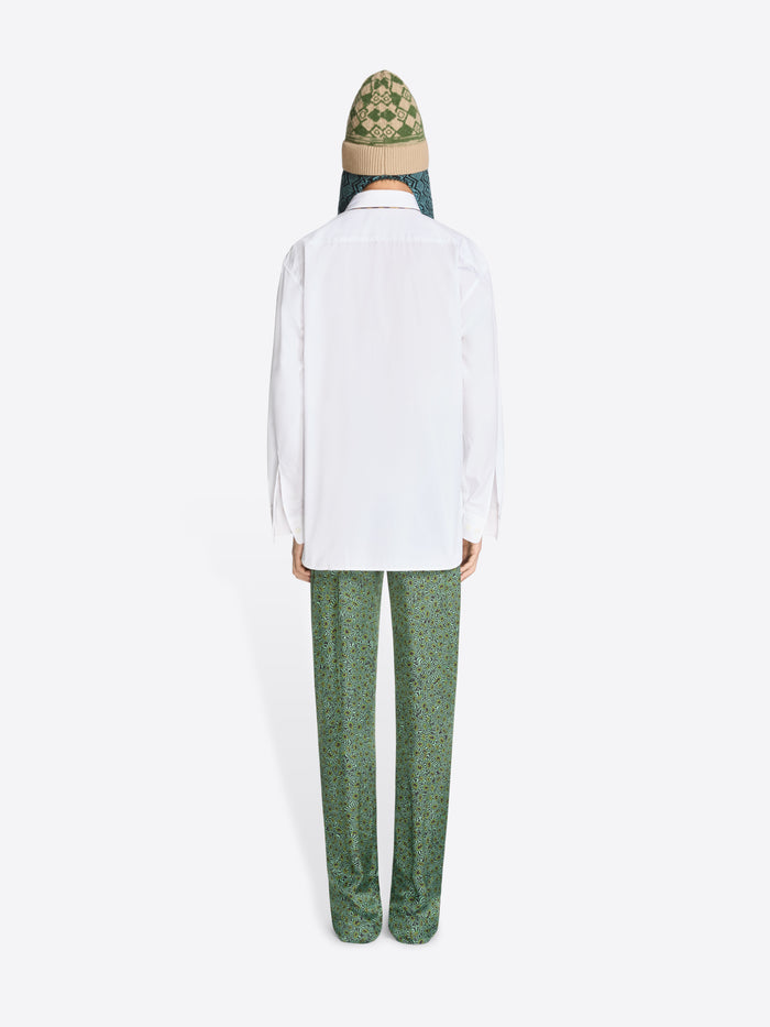 Back view of a person wearing a white shirt and green pants with a patterned hat on a white background