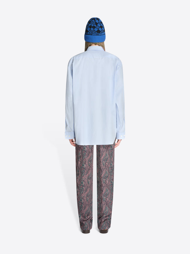 Back view of a person wearing a light blue shirt and patterned pants with a blue hat on a white background