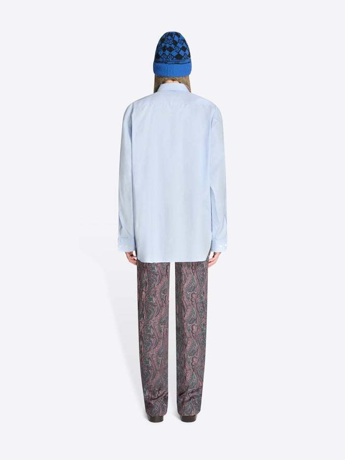 Back view of a person wearing a light blue shirt and patterned pants with a blue hat on a white background