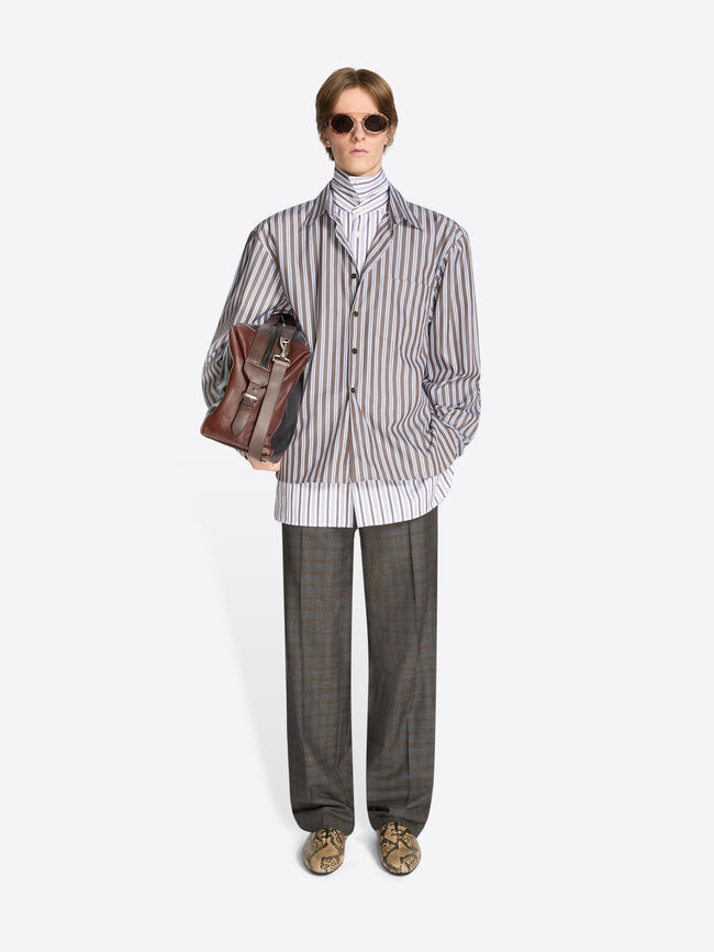 Person wearing a striped shirt, checkered pants, and holding a leather bag on a white background