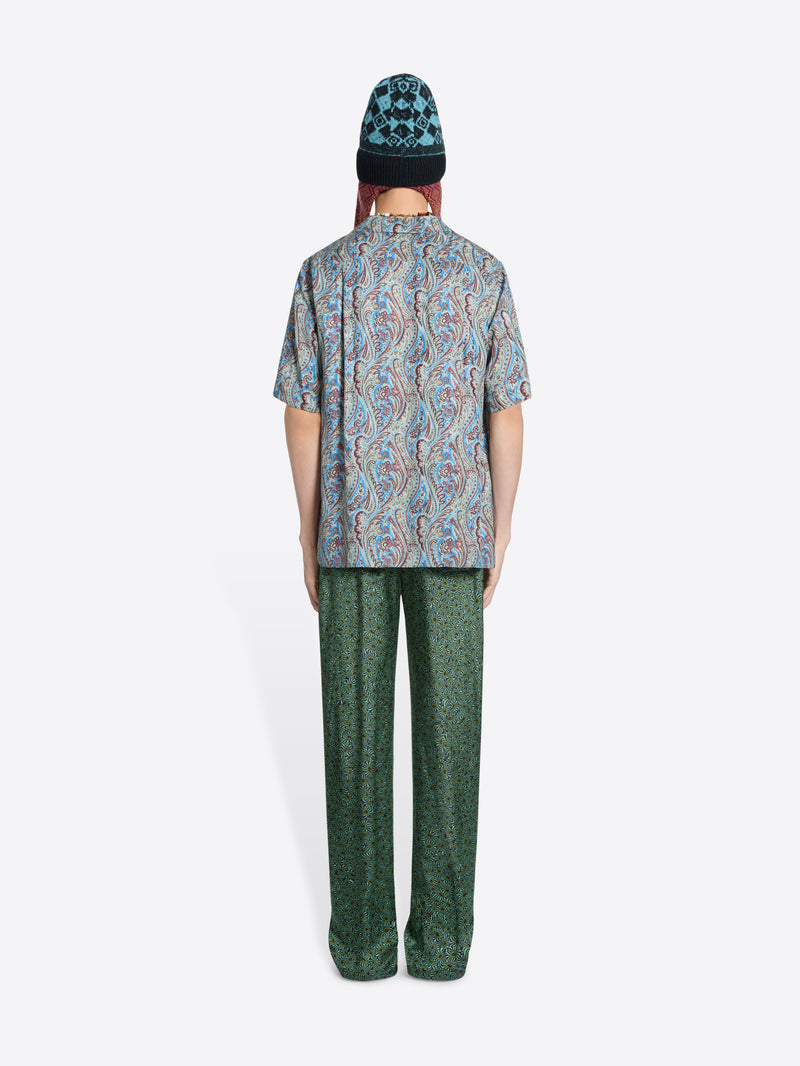 Back view of a person wearing a paisley-print short-sleeve shirt, patterned pants and a knit hat on the white background