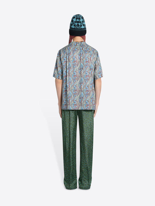 Back view of a person wearing a paisley-print short-sleeve shirt, patterned pants and a knit hat on the white background