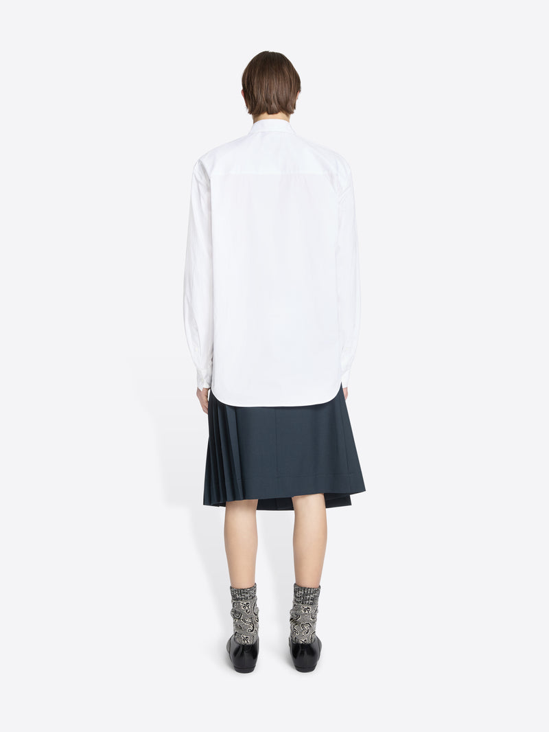 Back view of a person wearing a white shirt with a tie and dark skirt on a white background