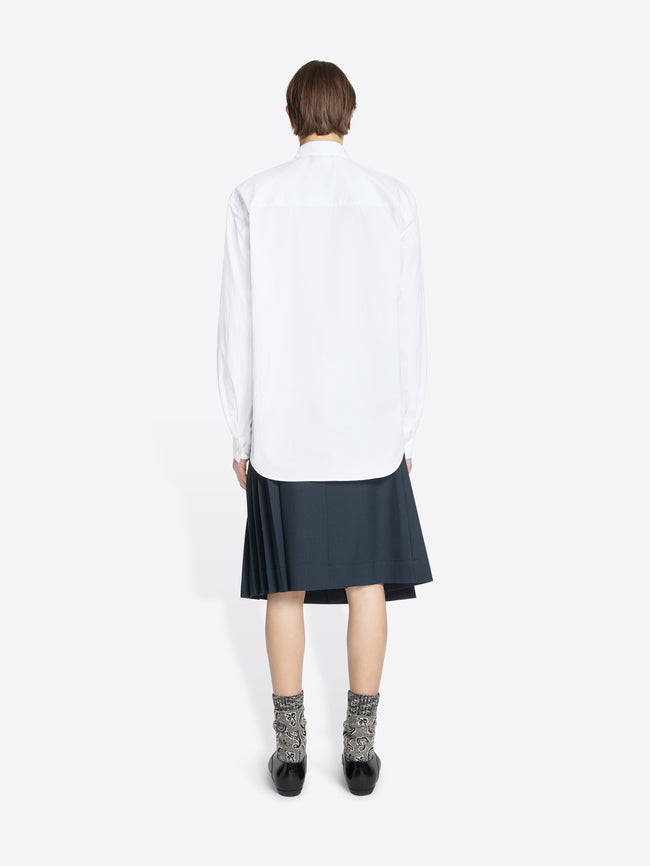 Back view of a person wearing a white shirt with a tie and dark skirt on a white background
