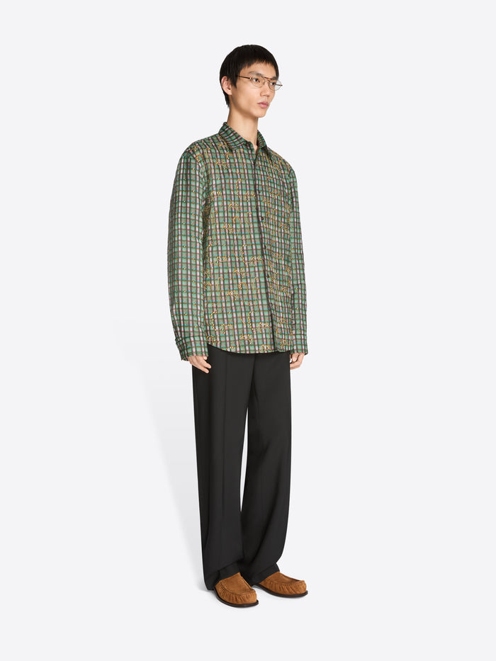 Man wearing a green plaid shirt and dark pants holding on a white background