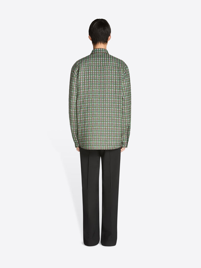 Man wearing a green plaid shirt and dark pants on a white background