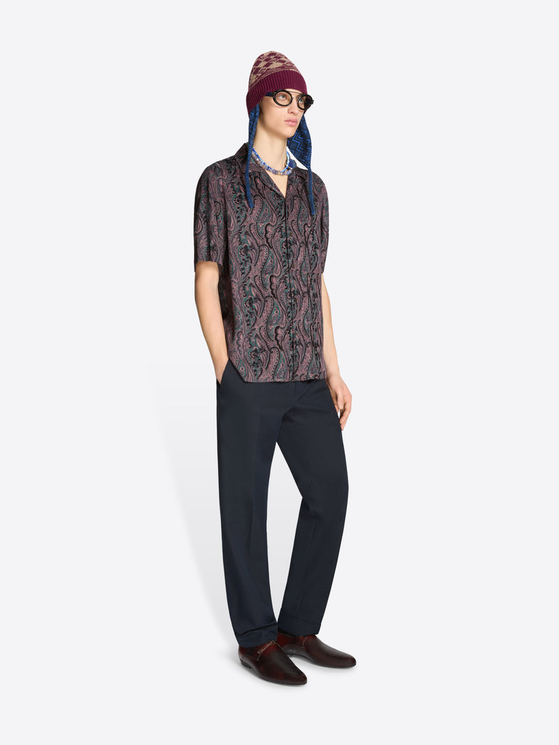 Person wearing a patterned shirt, dark pants and a hat on a white background