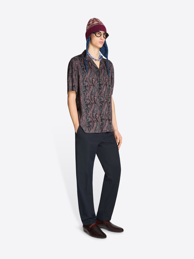 Person wearing a patterned shirt, dark pants and a hat on a white background