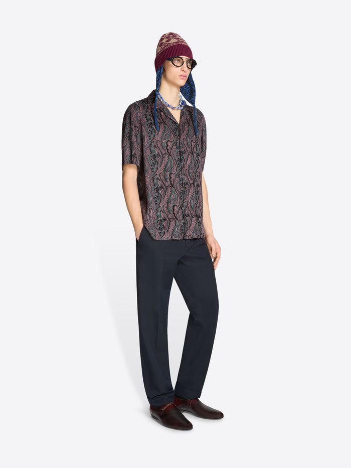 Person wearing a patterned shirt, dark pants and a hat on a white background