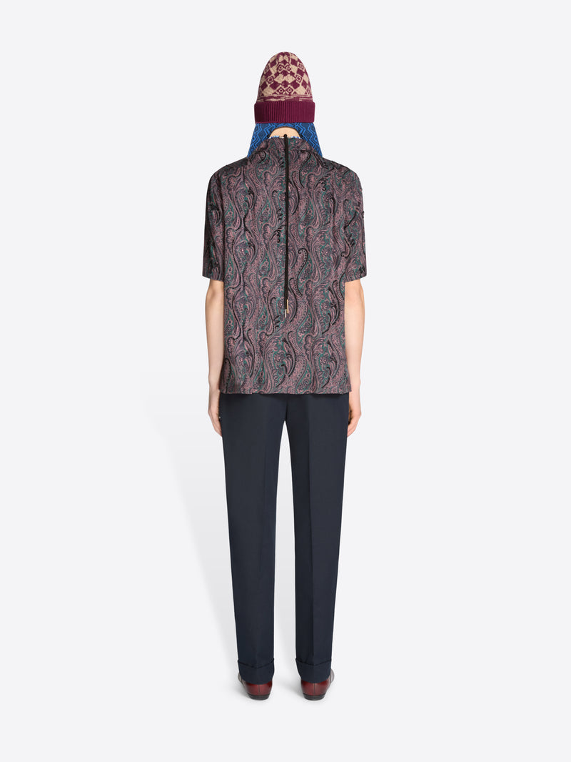 Back view of a person wearing a patterned shirt, dark pants with a hat on a white background
