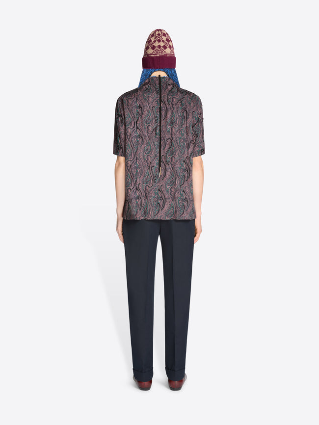 Back view of a person wearing a patterned shirt, dark pants with a hat on a white background