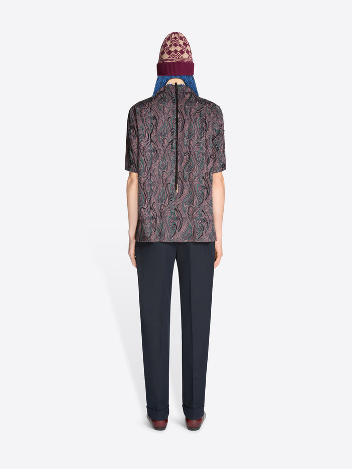 Back view of a person wearing a patterned shirt, dark pants with a hat on a white background