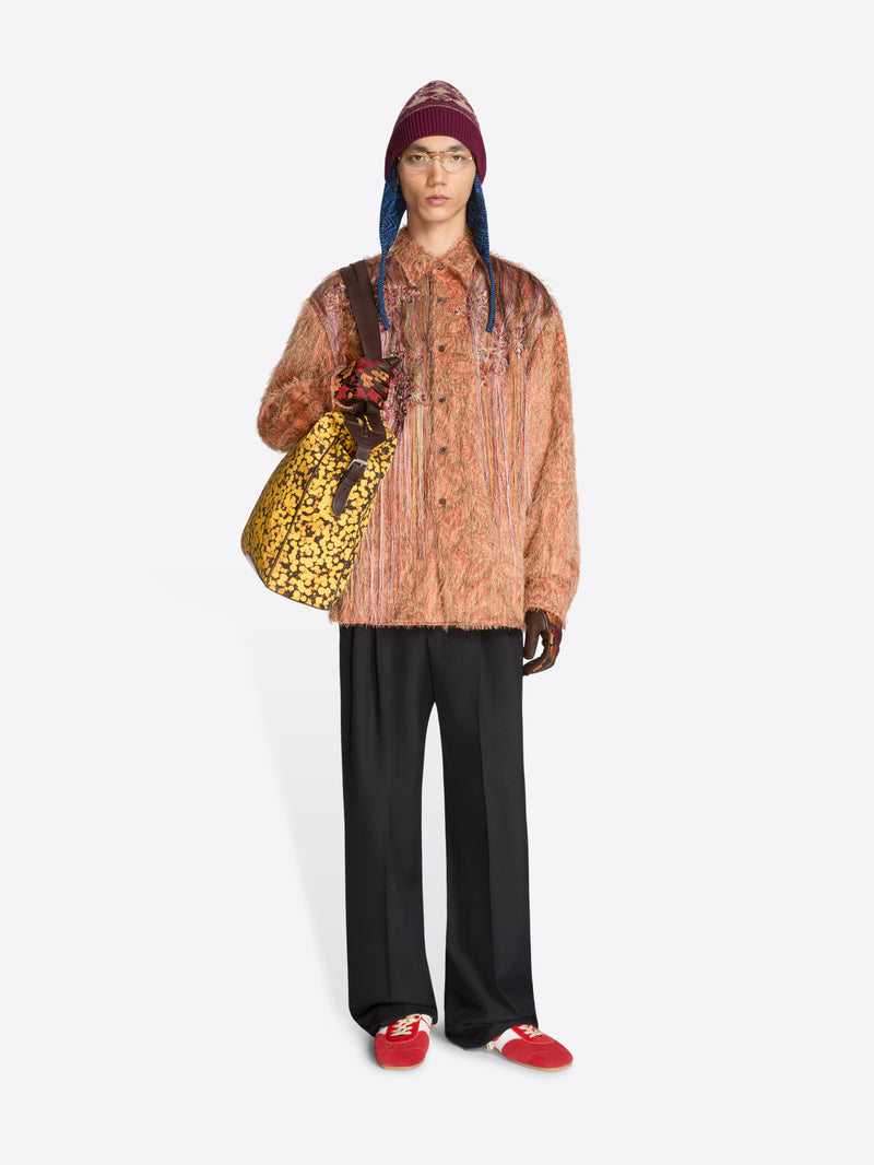 Person wearing a patterned shirt, black pants, and red shoes with a colorful bag on a white background