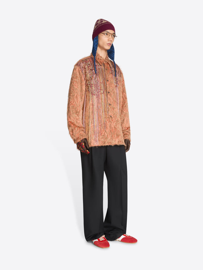Person wearing a patterned shirt, black pants, and red shoes on a white background