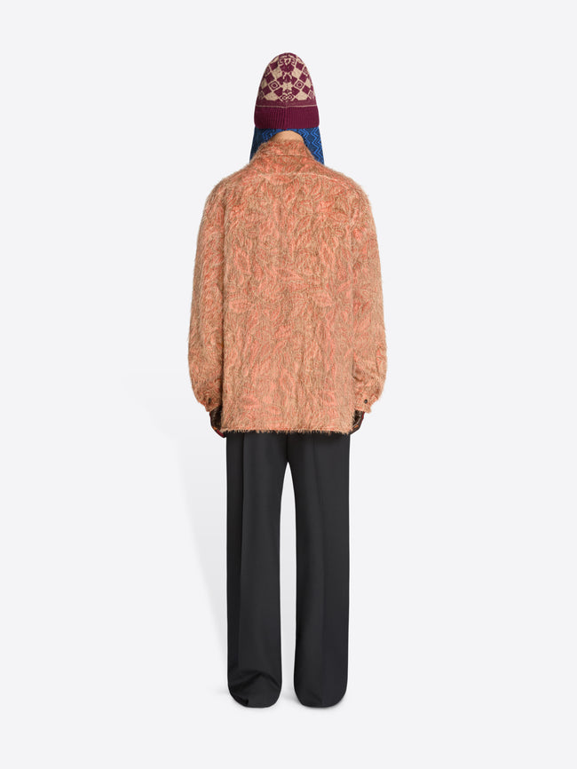 Back view of a person wearing a textured shirt, black pants and hat on a white background