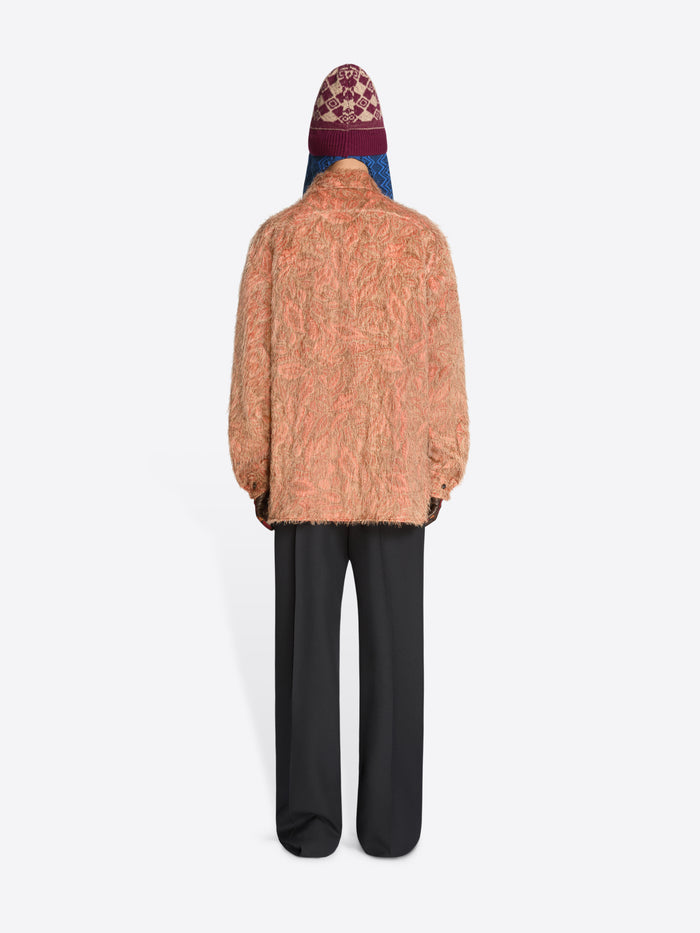 Back view of a person wearing a textured shirt, black pants and hat on a white background