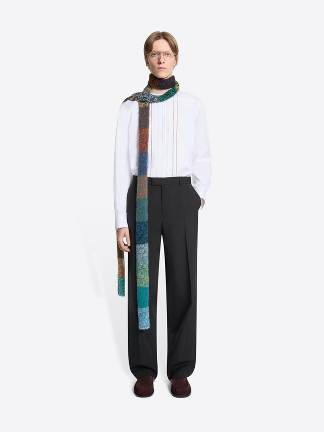 Person wearing a white shirt, black pants, and a colorful scarf on a white background