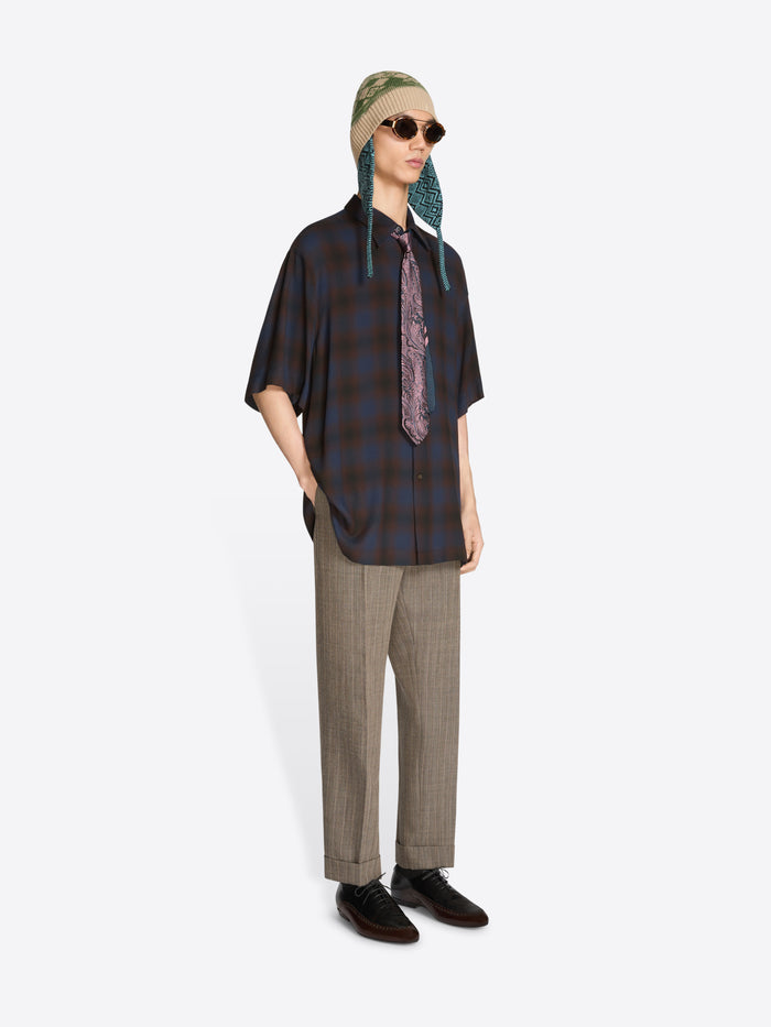 Person wearing a plaid shirt, patterned tie, pants, hat and sunglasses on a white background