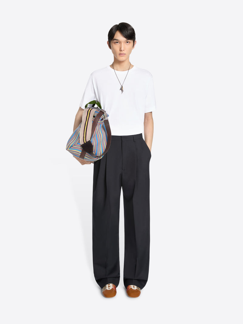 Person wearing a white t-shirt, wide-leg navy trousers, carrying a striped bag on a white background 