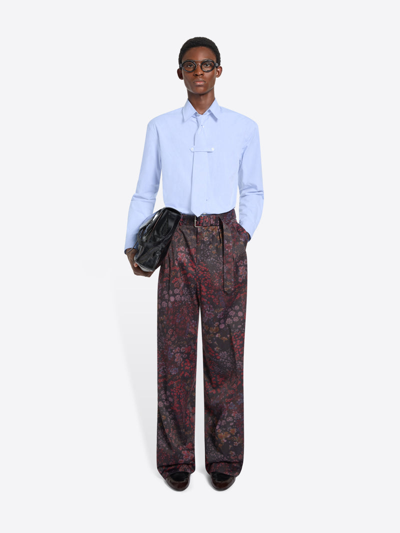 Person wearing a light blue shirt and patterned pants holding a black bag on a white background
