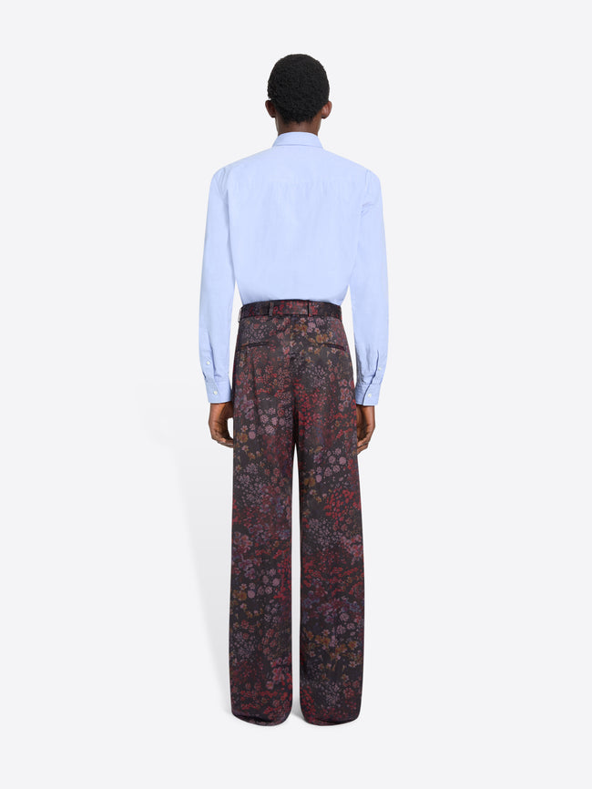 Back view of a person wearing a light blue shirt and patterned pants on a white background