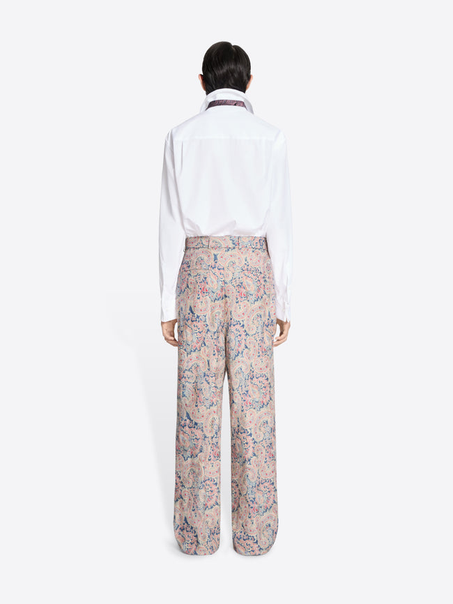 Back view of a person wearing a white shirt and floral pants on a white background