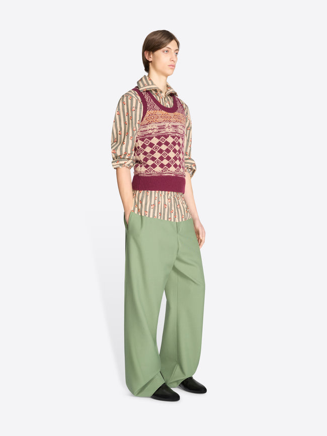 Person wearing a patterned vest and green pants on a white background