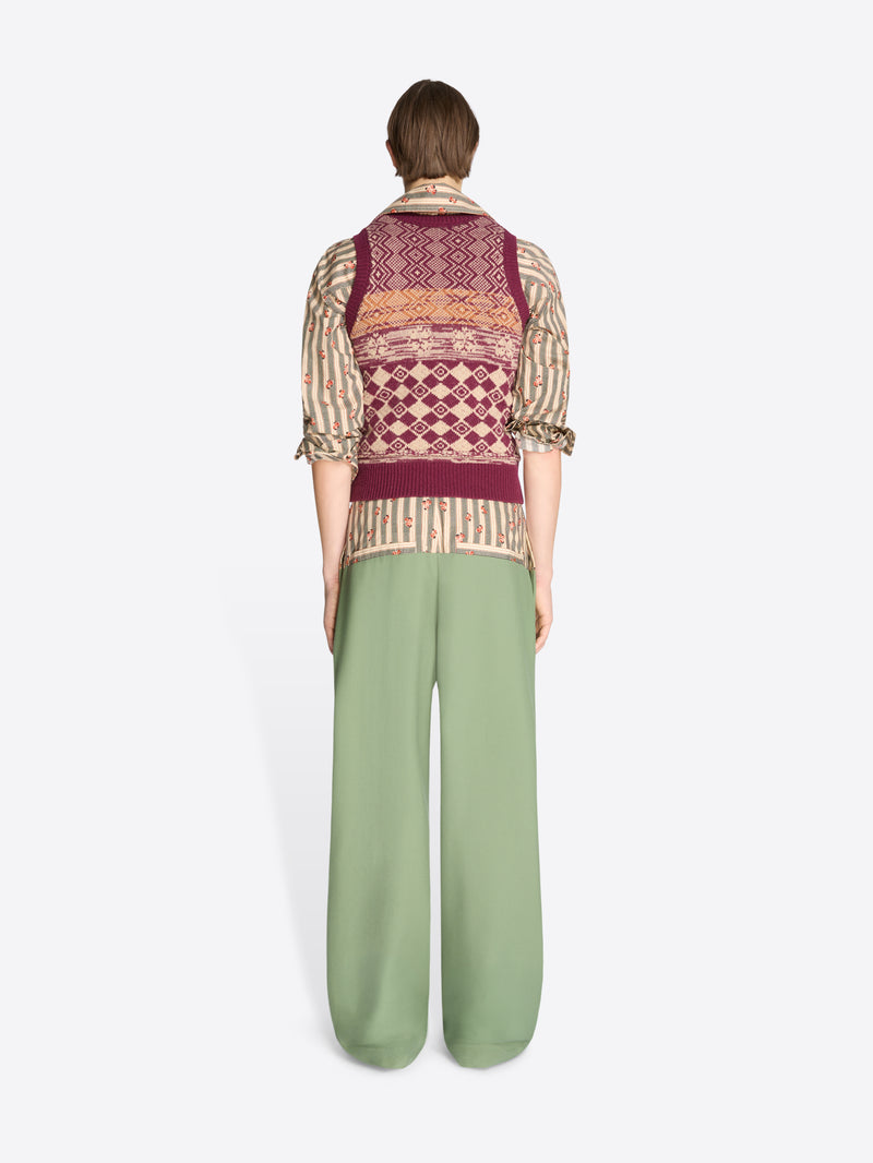 Back view of a person wearing a patterned vest and green pants on a white background