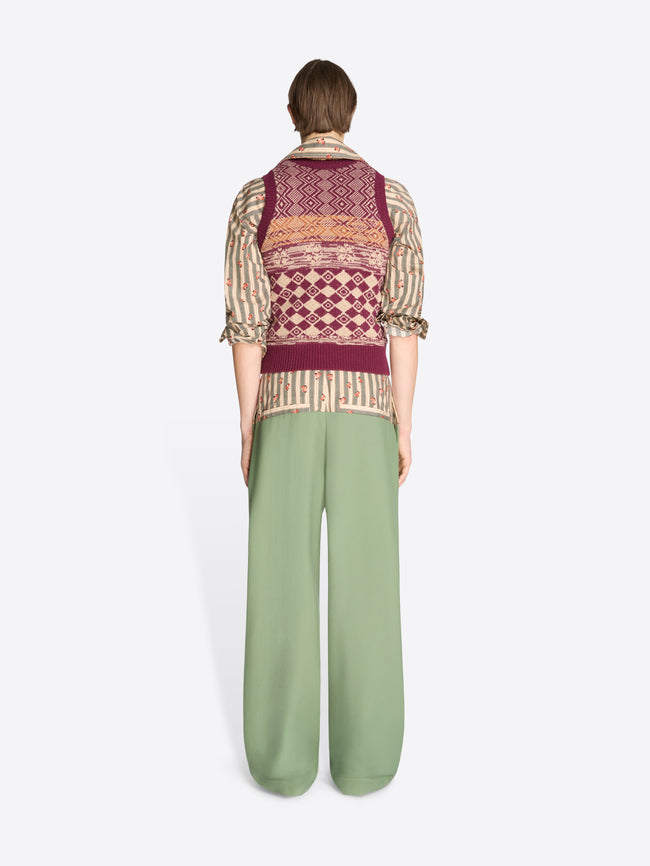 Back view of a person wearing a patterned vest and green pants on a white background