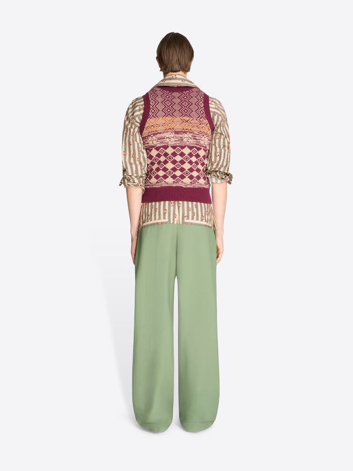 Back view of a person wearing a patterned vest and green pants on a white background