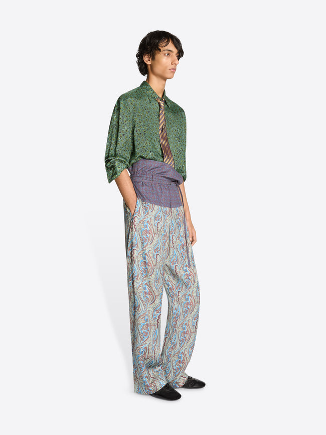 Person wearing a green shirt, patterned tie, and colorful pants with a purple waistband on a white background