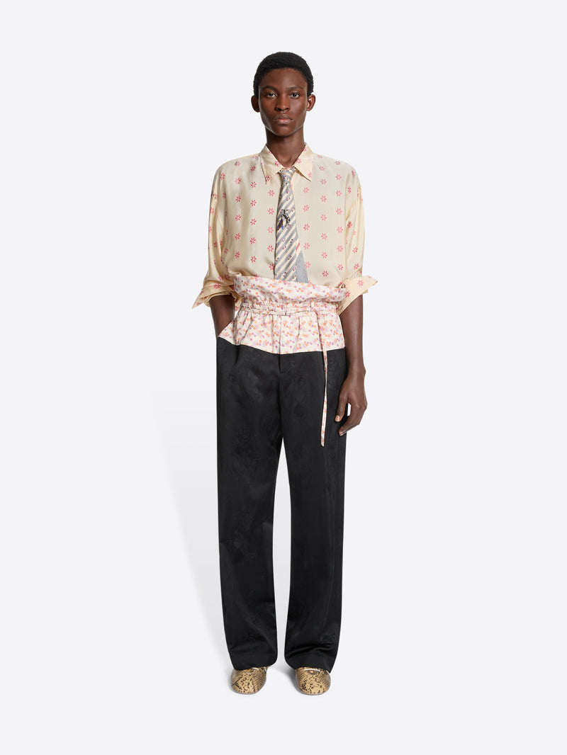 Person wearing a patterned shirt and black pants with a floral waistband on a white background