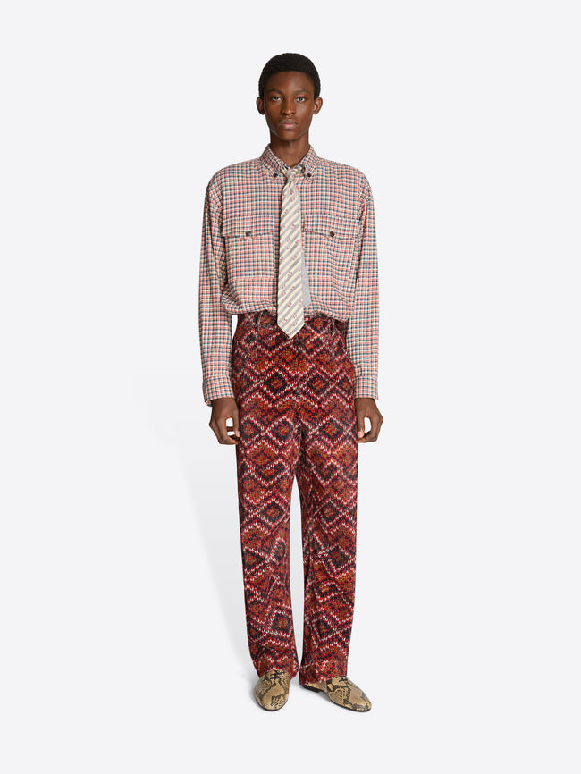 Person wearing a patterned shirt and red pants on a white background