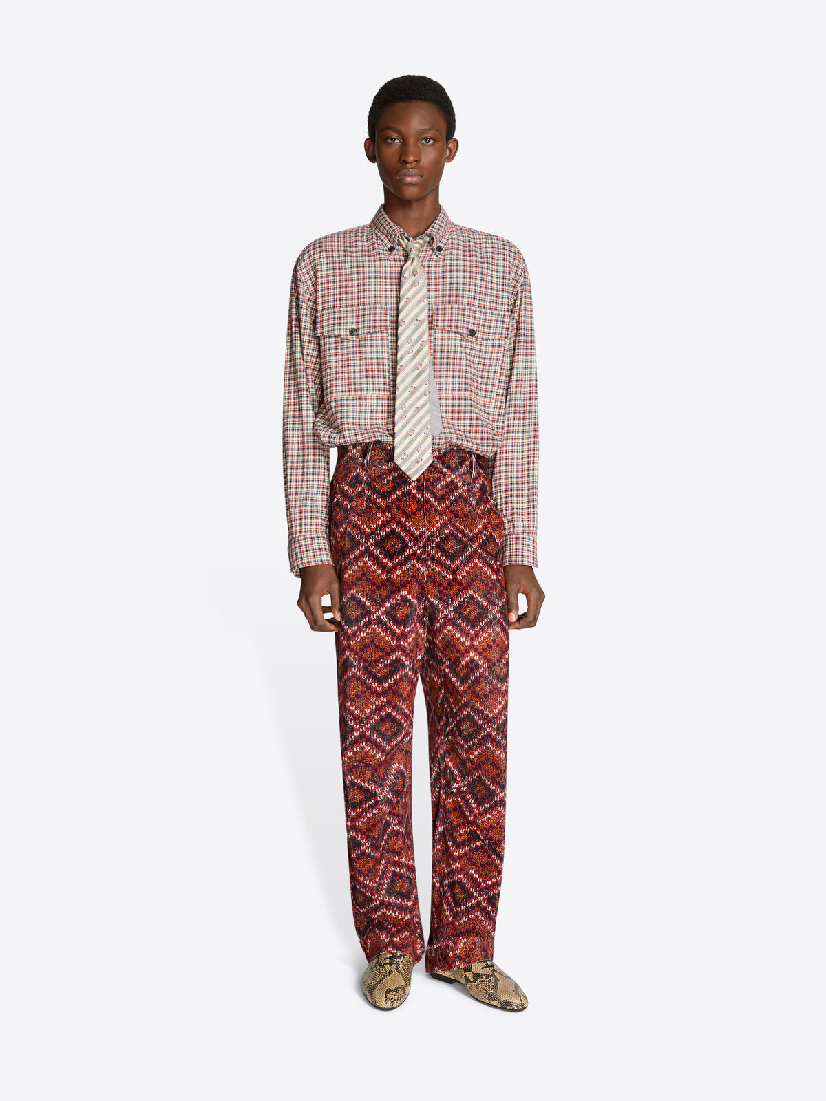 Person wearing a patterned shirt and red pants on a white background