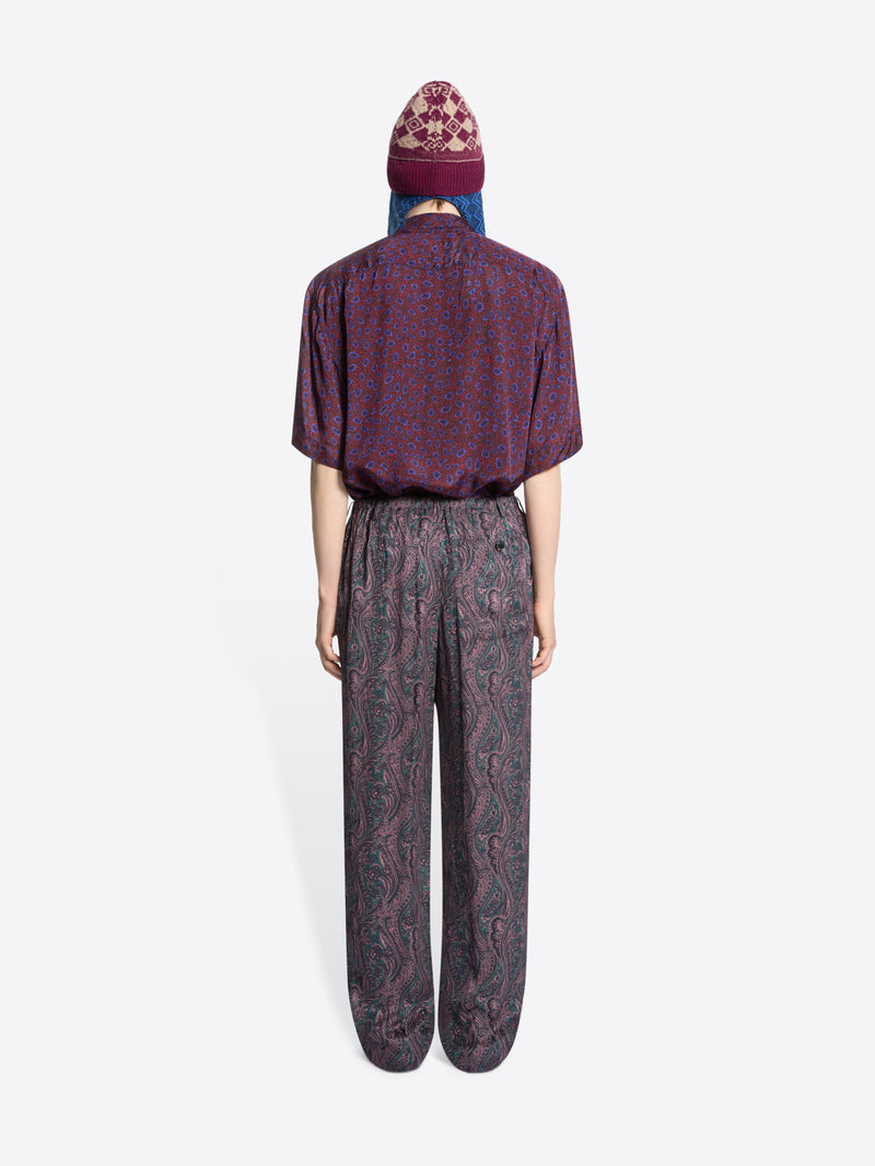 Back view of a person wearing a patterned shirt and pants, a hat on a white background