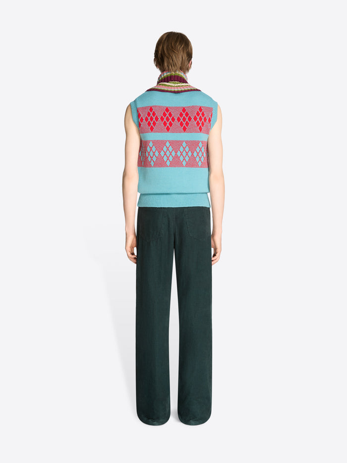 Back view of a person wearing a sleeveless vest with a geometric pattern and dark green pants on a white background