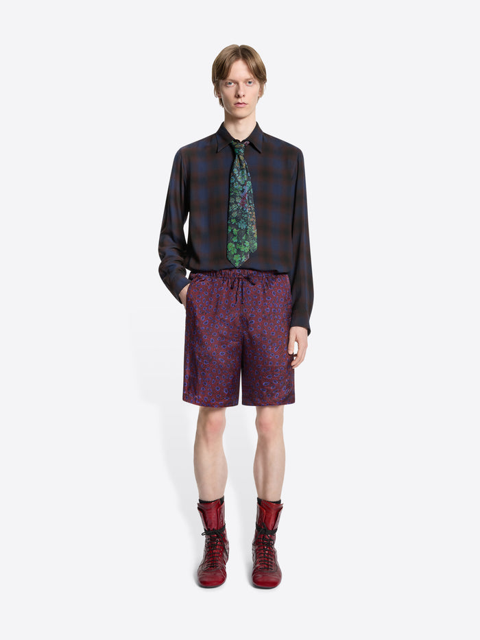 Person wearing a patterned shirt, tie, and shorts with red boots on a white background
