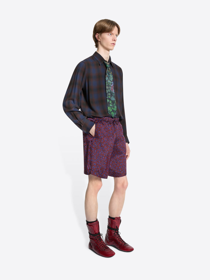 Person wearing a patterned shirt, tie, and shorts with red boots on a white background
