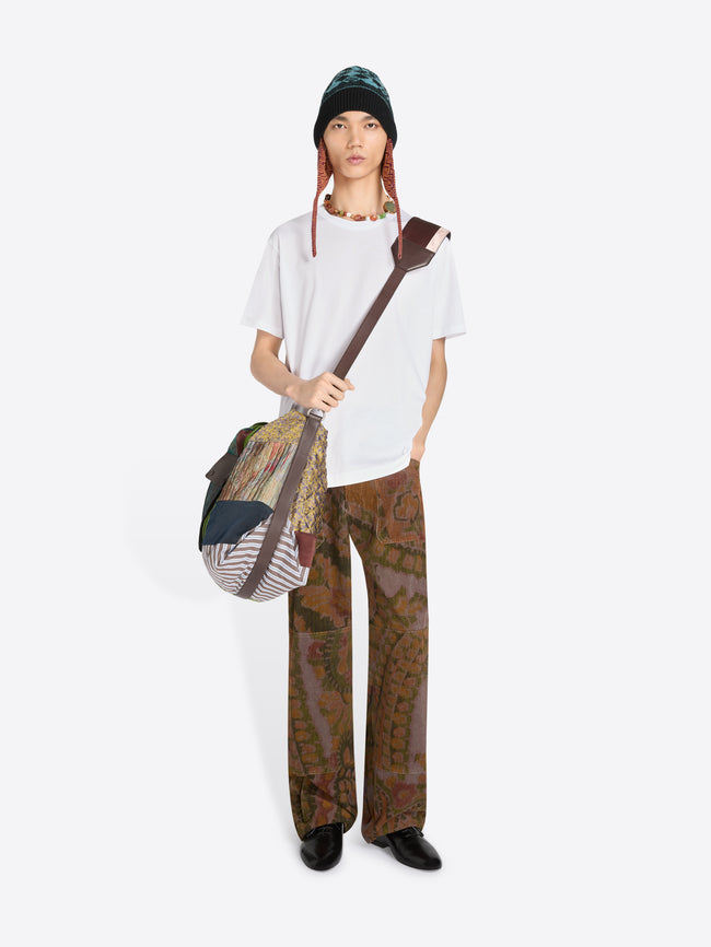 Person wearing a white t-shirt, patterned pants, and a hat, holding a bag on a white background