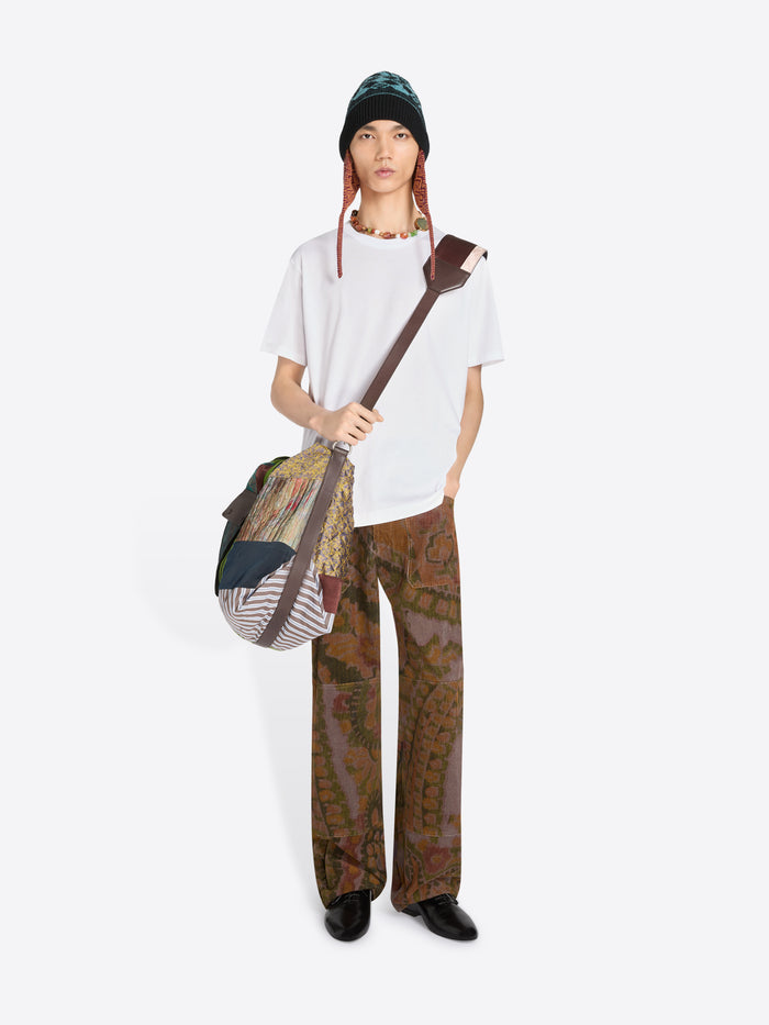 Person wearing a white t-shirt, patterned pants, and a hat, holding a bag on a white background