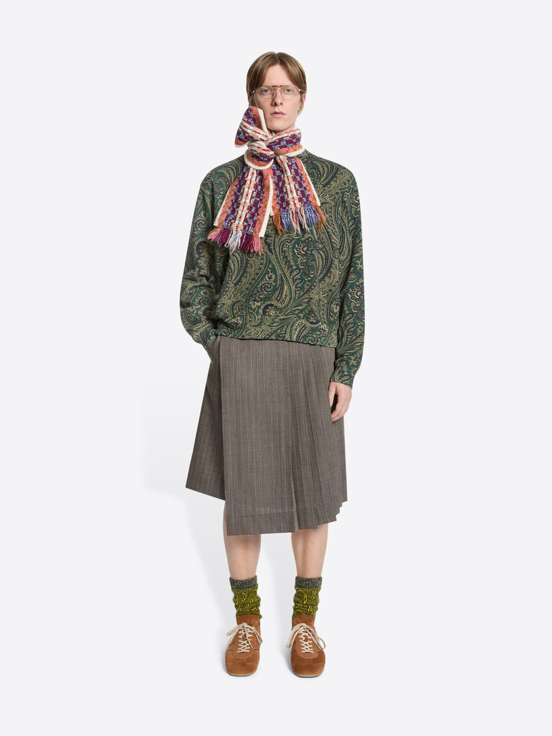 Person wearing a patterned sweater, scarf, and skirt on a white background