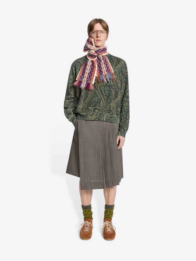 Person wearing a patterned sweater, scarf, and skirt on a white background