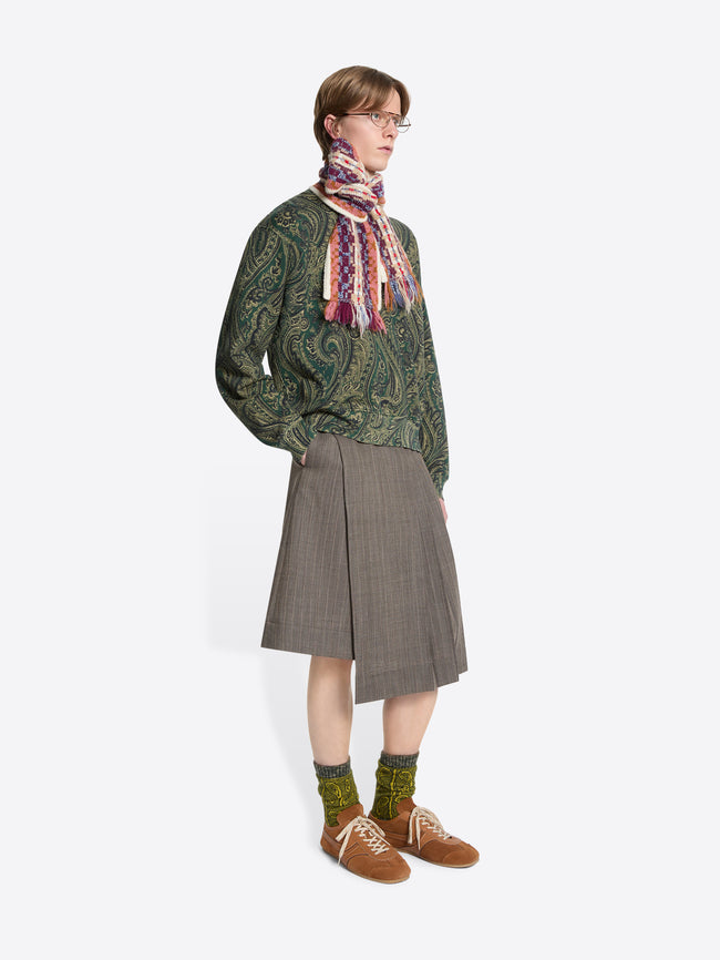 Person wearing a green patterned sweater, skirt, scarf and brown shoes on a white background
