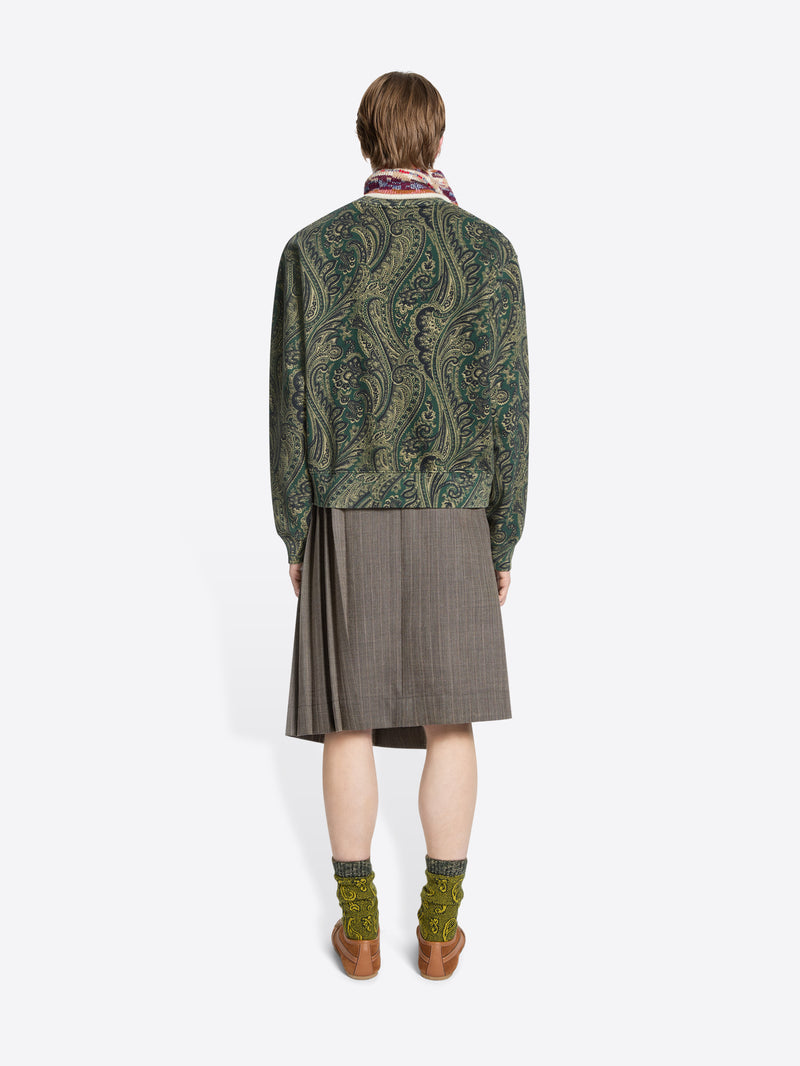Back view of a person wearing a green patterned sweater and skirt on a white background