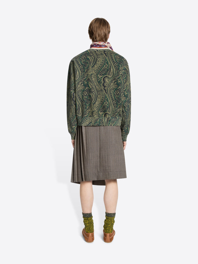 Back view of a person wearing a green patterned sweater and skirt on a white background