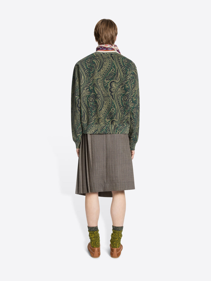 Back view of a person wearing a green patterned sweater and skirt on a white background