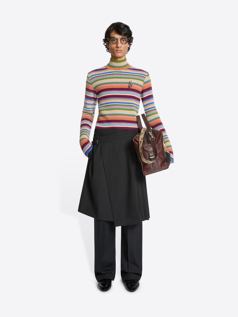 Person wearing a colorful striped sweater, black skirt and black pants with a brown bag on a white background