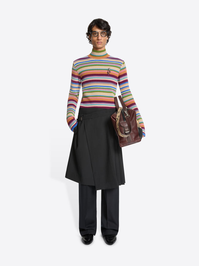 Person wearing a colorful striped sweater, black skirt and black pants with a brown bag on a white background