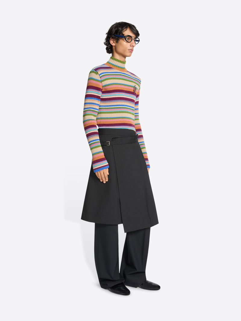 Person wearing a colorful striped sweater, black skirt and black pants on a white background
