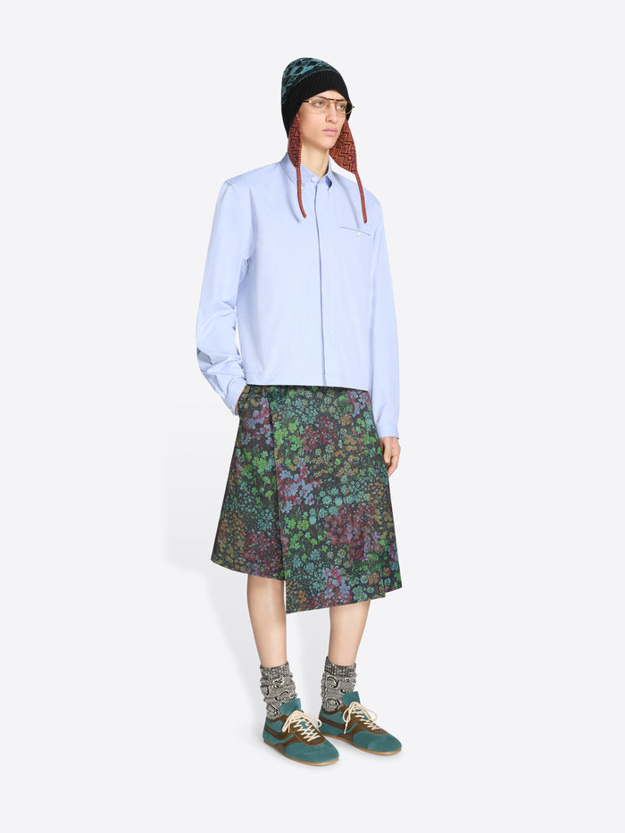 Person wearing a light blue shirt, patterned floral skirt, and green hat on a white background